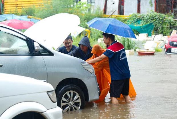 Nhiều người d&acirc;n đang nỗ lực đội mưa để di chuyển chiếc xe ra khỏi biển nước